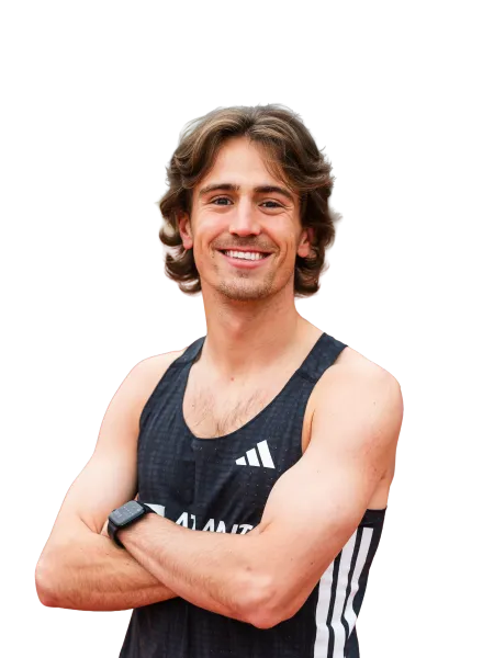 Smiling young male athlete with wavy hair wearing a black Adidas sports tank top and smartwatch, arms crossed.