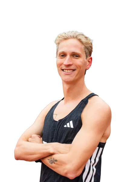 Smiling young man with crossed arms wearing a black Adidas tank top and showing a tattoo on his forearm.