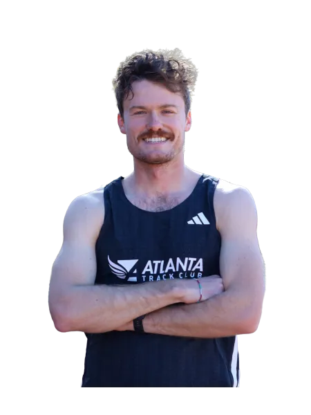 Smiling male athlete with curly hair wearing Atlanta Track Club black sleeveless top, arms crossed