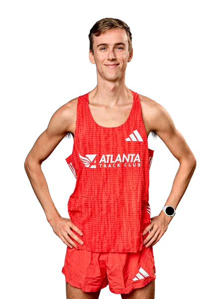 Smiling male athlete in red Atlanta Track Club running uniform with smartwatch posing hands on hips.