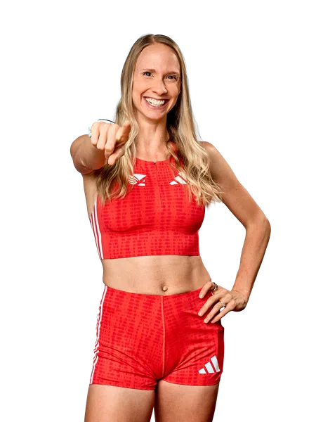 Smiling athletic woman in red sportswear pointing forward with one hand on her hip, isolated on black.