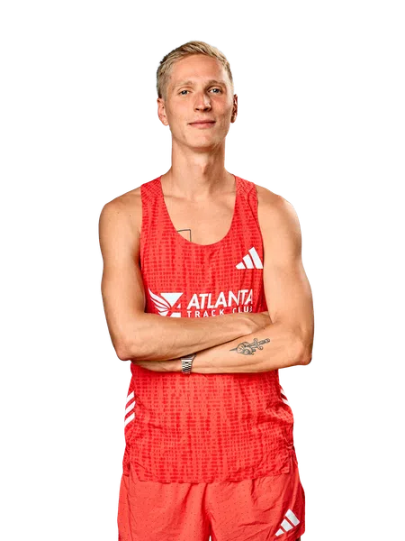 Young male athlete in red Atlanta Track Club running gear with tattoos and short blonde hair crossing arms