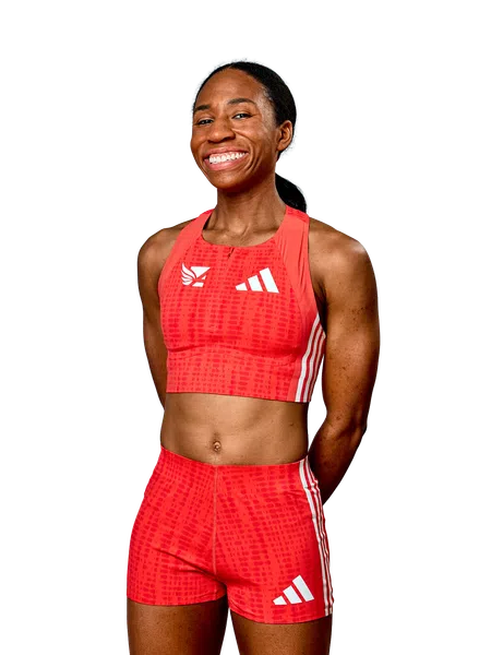 Smiling female athlete in red Adidas sports top and shorts posing confidently on a white background.
