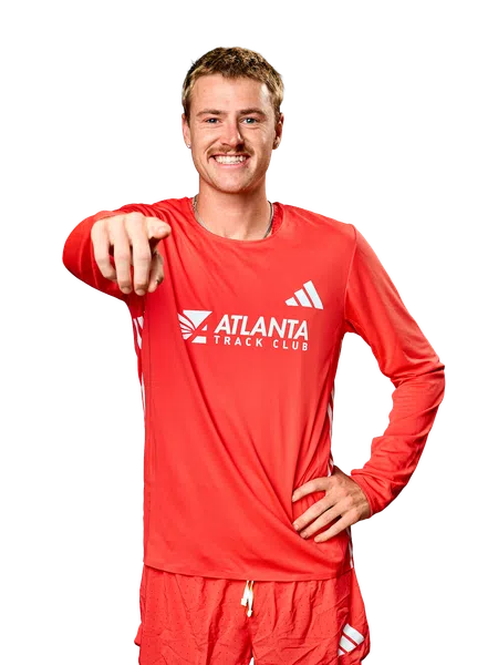 Smiling male athlete in red Atlanta Track Club outfit pointing forward with hand on hip against black background