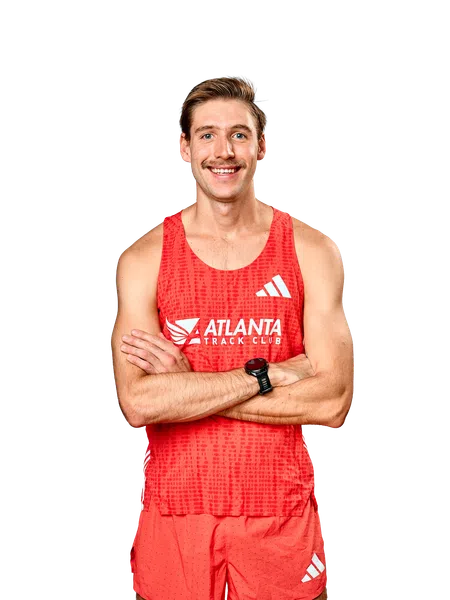 Smiling male athlete wearing red Atlanta Track Club running outfit with a watch, arms crossed.