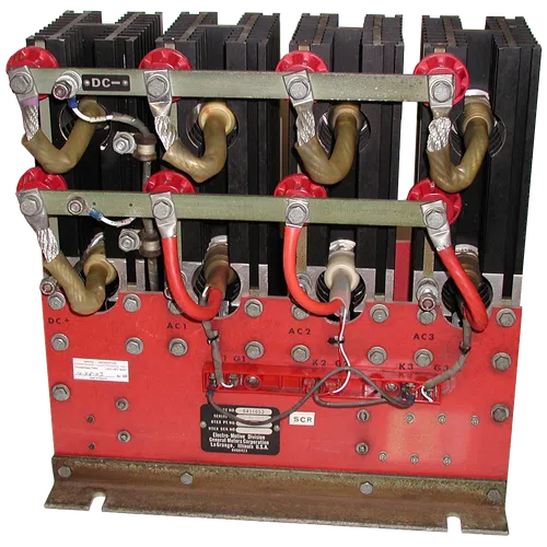 Industrial electrical component with coils, red and black wiring, mounted on a red metal base with labels.