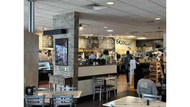 Busy Brooklyn cafe interior with customers, menu boards, modern decor, and seating area with tables and chairs.