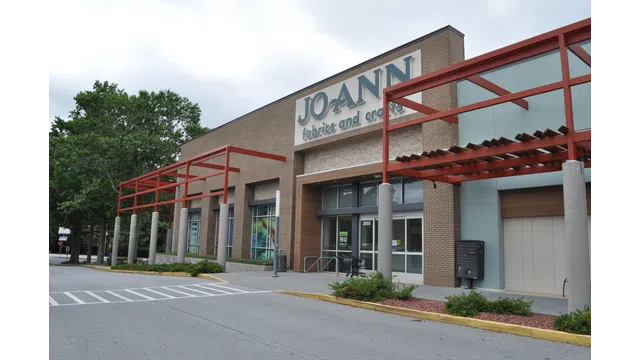 Exterior view of JOANN fabrics and crafts store with brick facade and red pergola on a cloudy day