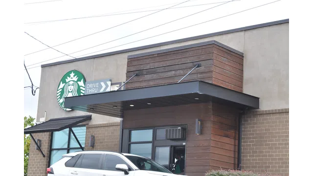 Starbucks coffee shop exterior with drive-thru lane and a white SUV parked nearby during daytime.