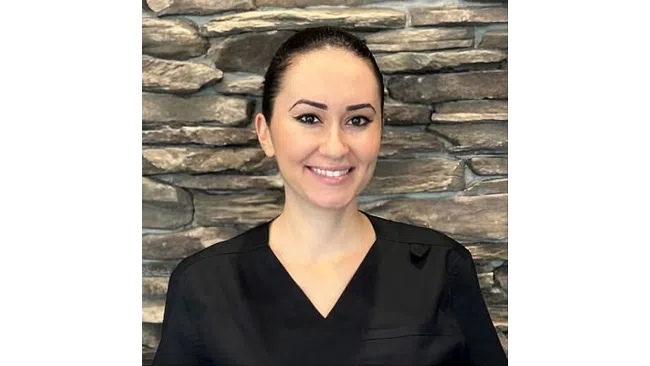 Smiling woman in black medical scrubs stands in front of a stone wall background
