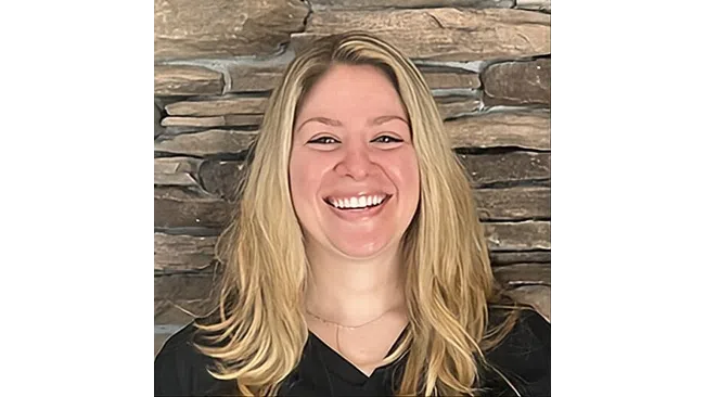 Smiling woman with long blonde hair in front of a textured stone wall background