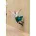 Man in green tartan kilt jumping energetically against a beige concrete wall outdoors.