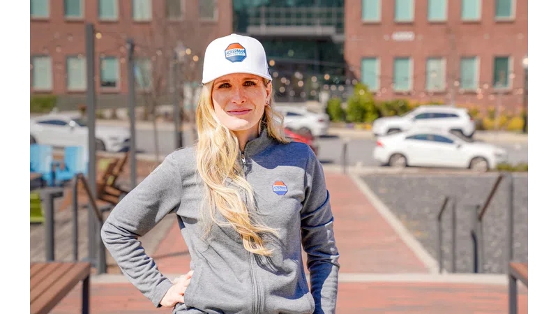 Smiling woman in branded cap and jacket stands outdoors, showcasing a modern urban setting.