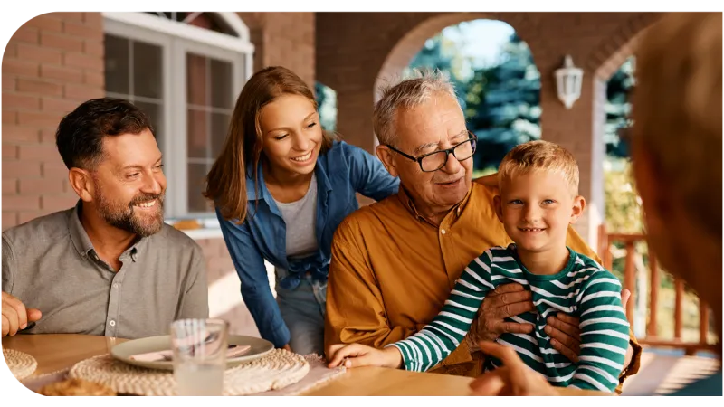 Happy multigenerational family enjoying time together outdoors at a wooden table on the porch.