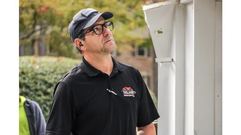 Man wearing black uniform with Nelson logo inspects white building exterior during daytime
