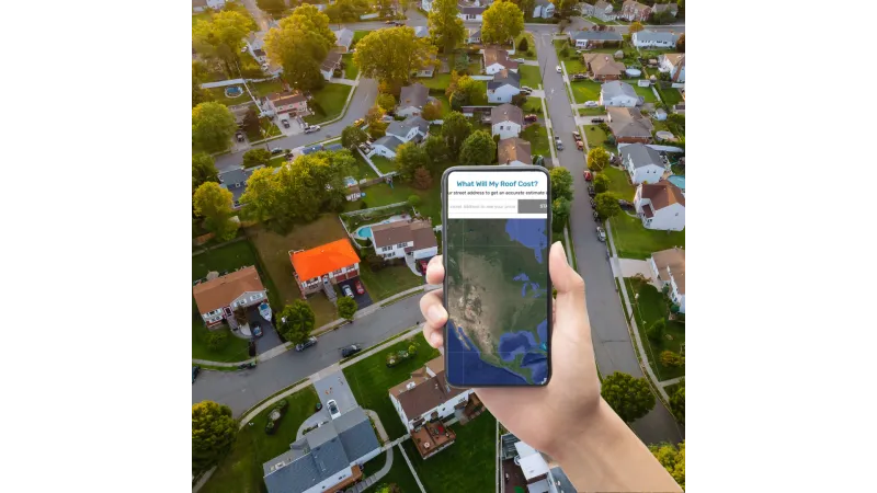Hand holding smartphone showing roof cost estimator app over aerial view of suburban neighborhood with many houses.