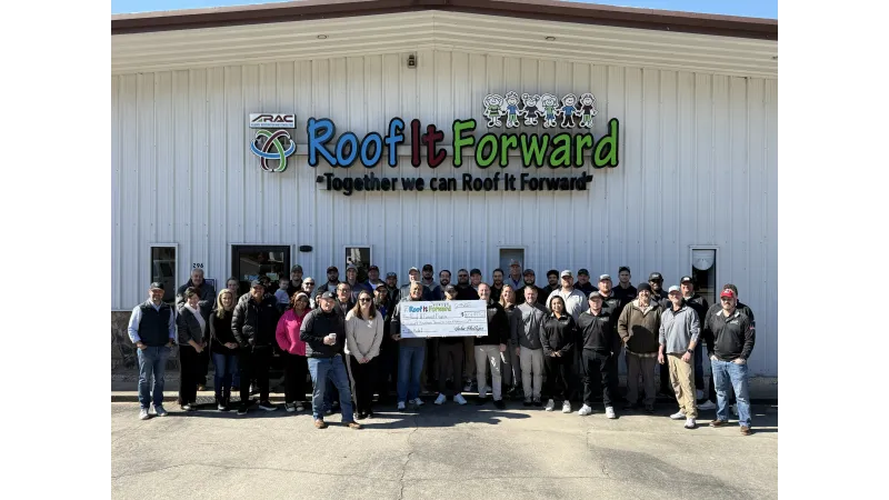 Group of people standing outside a building holding a large check under a Roof It Forward sign