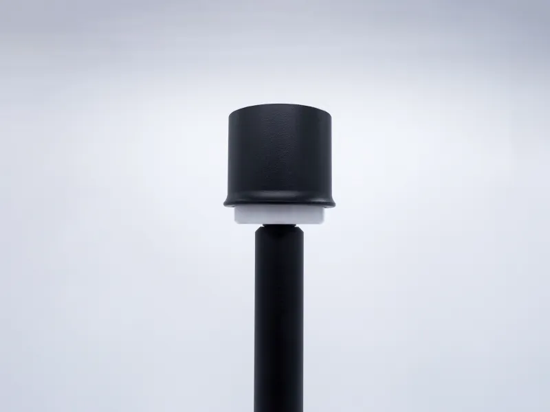 Black cylindrical modern outdoor garden lamp post with white LED diffuser on a plain gray background