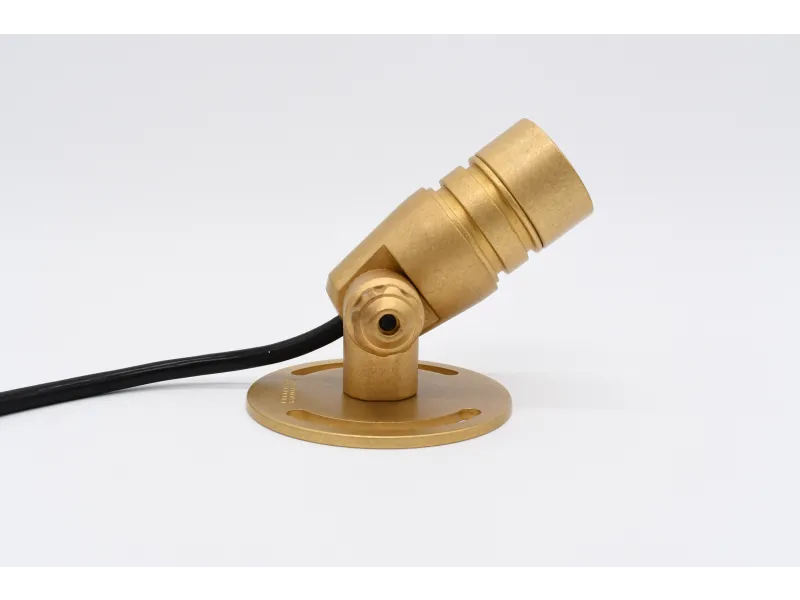 Brass spotlight fixture with adjustable head mounted on round base with attached black cable on white background