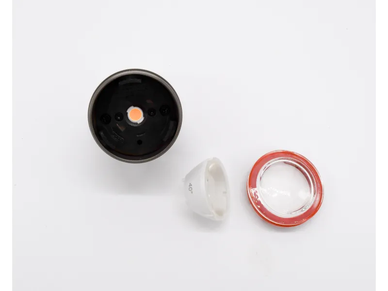 Disassembled LED light components including black base, white reflector, and clear lens with orange rim on white background.
