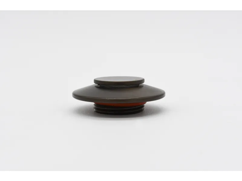 Dark metal round cap with flat top and red gasket lying on white surface.