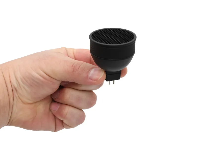 Hand holding a small black electronic sensor device with two metal pins against white background