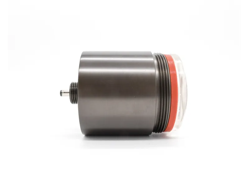 Close-up of a cylindrical metal component with threaded ends and a transparent cap with an orange seal.