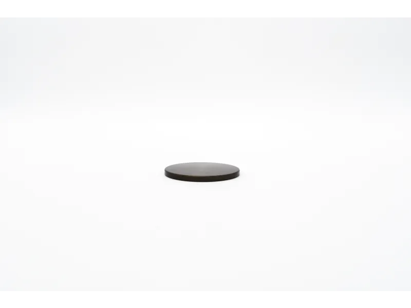Small round black disk placed on a white surface with a minimalist background.
