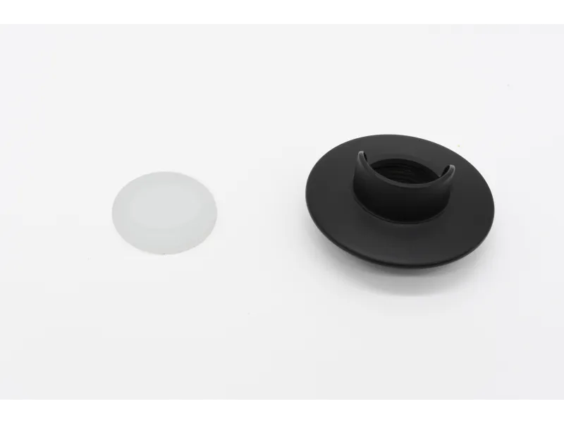 Black plastic threaded cap with attached collar and separate translucent white plastic sealing disc on white background