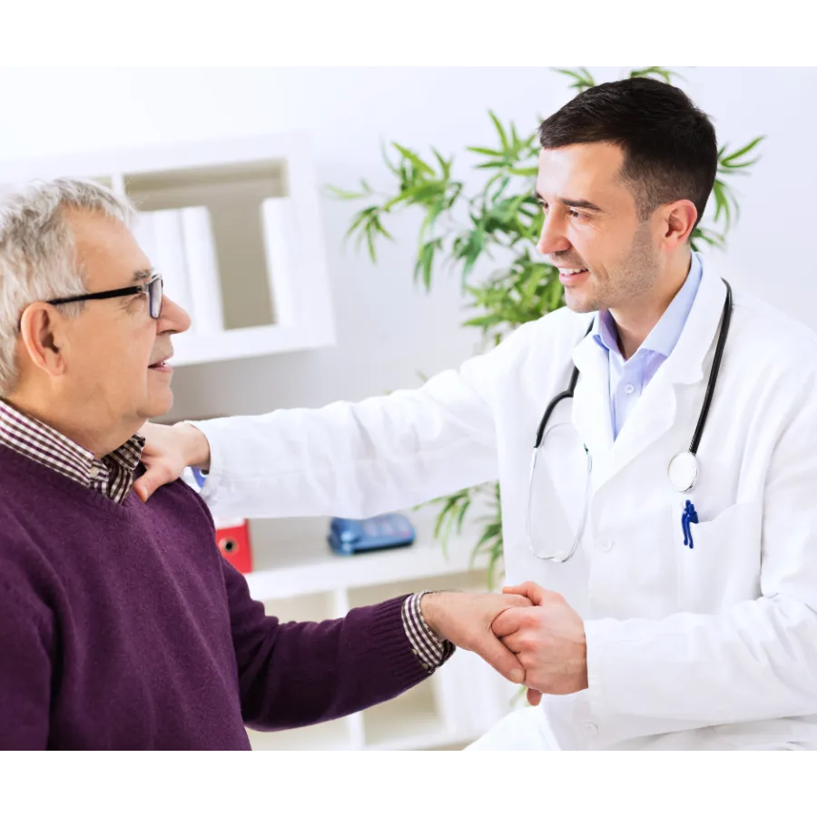 Doctor wearing white coat and stethoscope shakes hands with elderly patient in medical office.