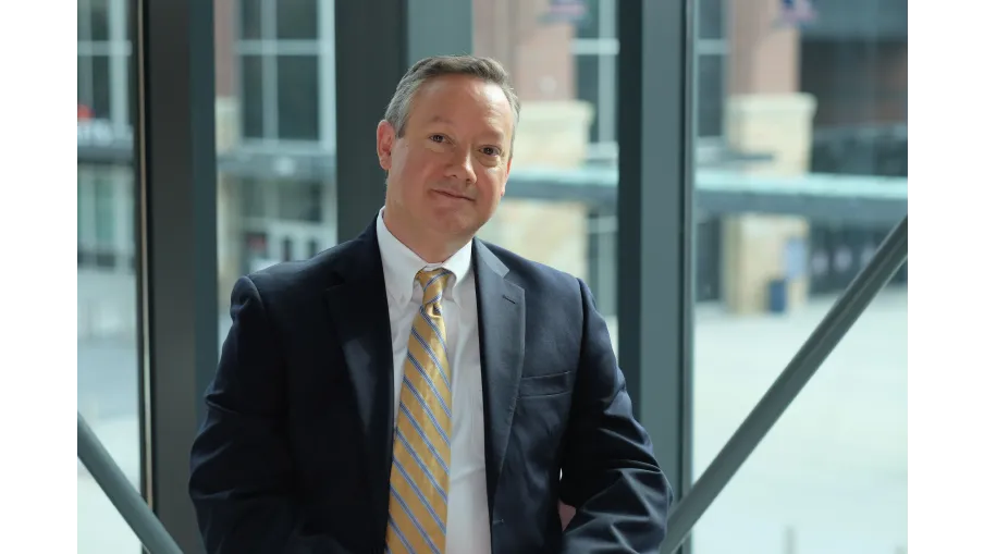 Middle-aged man in a suit with yellow striped tie sitting near large windows in a modern office building.