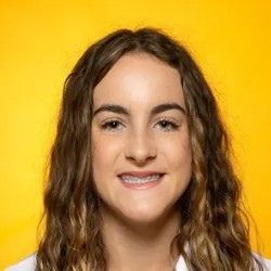 Smiling young woman with braces and curly hair against a bright yellow background
