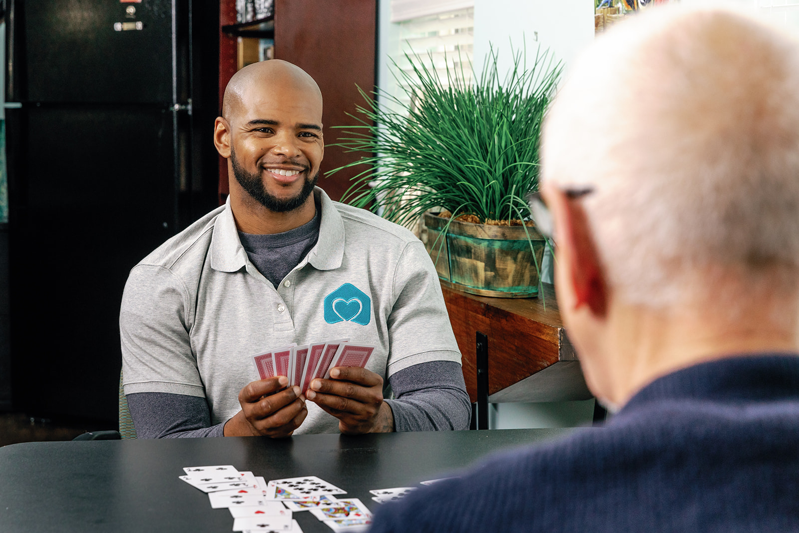 A smiling man playing cards with an elderly man in a cozy indoor setting.
