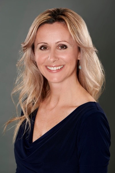 Smiling woman with blonde hair wearing a navy blue top against a plain gray background.