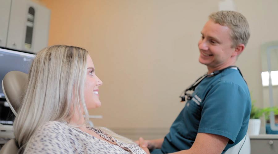 Dentist smiling and talking with a female patient in a dental clinic setting showing friendly interaction