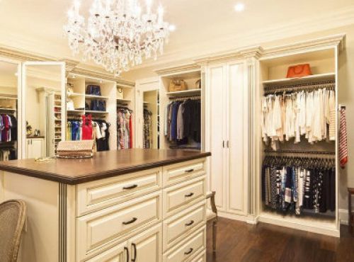 A luxurious walk-in closet with cream-colored cabinets and a chandelier