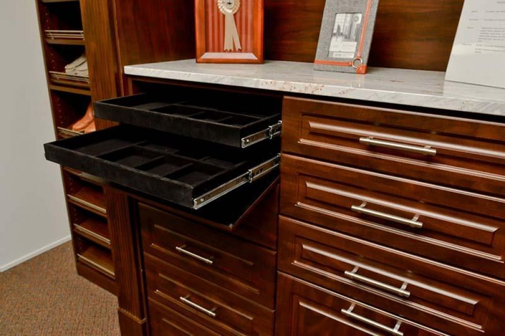 A closet system with rich brown wood has narrow drawers for jewelry.