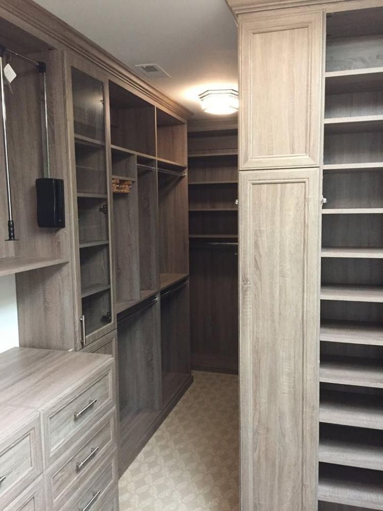 A large walk-in closet system in light brown has shoe racks, drawers, and hanging racks.