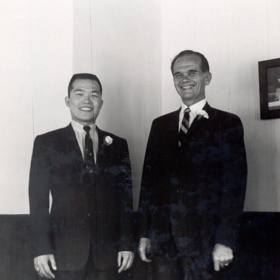 Koji and Bertrand stand next to each other at Koji's wedding