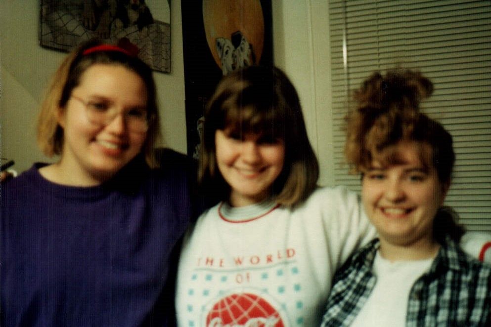 Three girls stand together in a college dorm