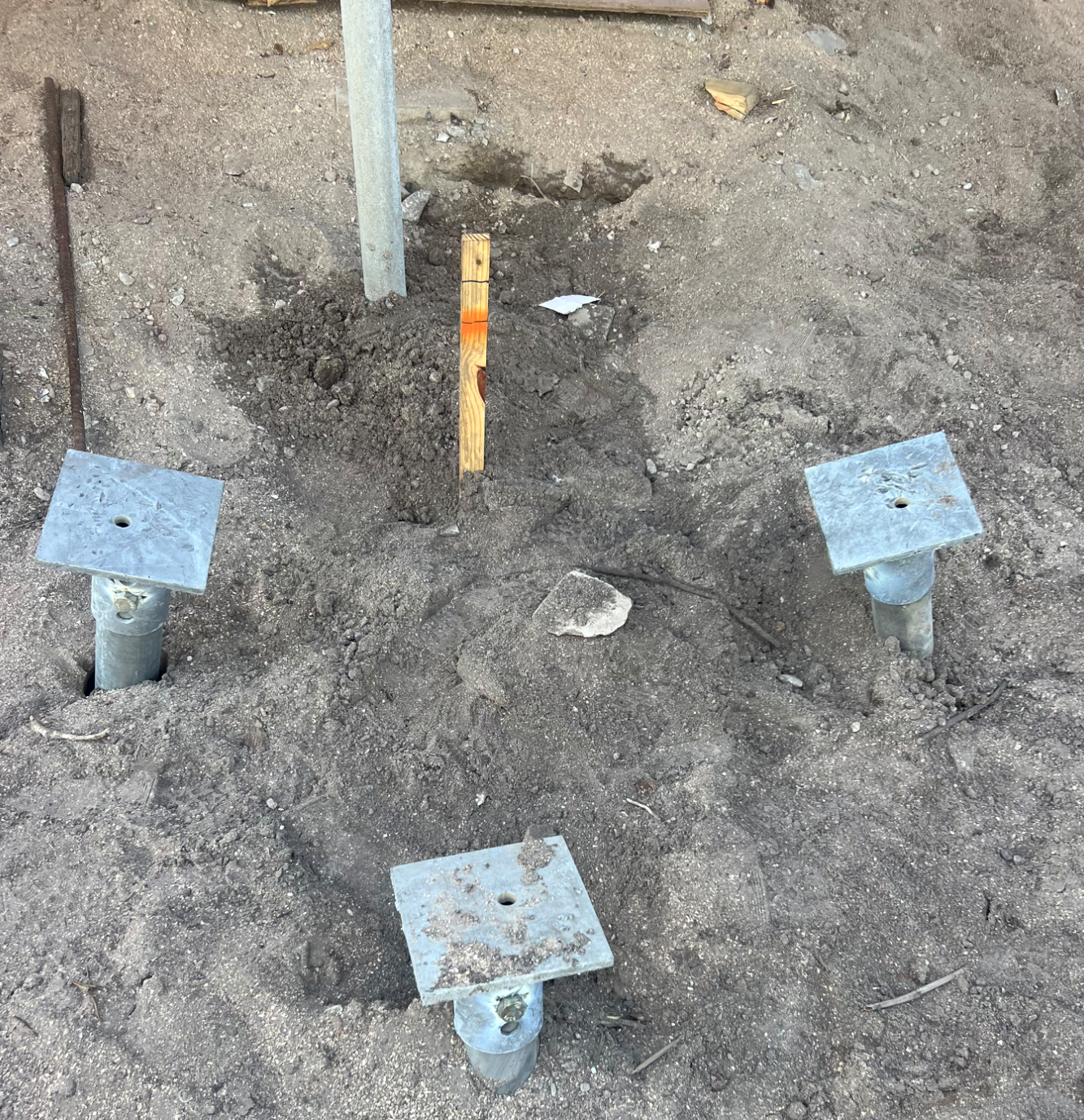 Metal foundation anchors partially buried in dirt for construction footing supports on a building site.