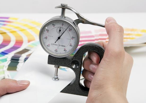 A person using a thickness gauge to measure a paper's caliper