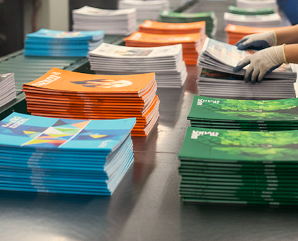 A commercial print shop worker placing colorfully printed booklets into stacks