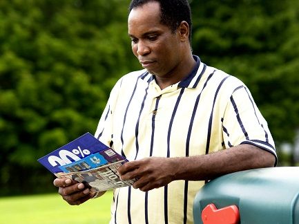 A man leaning on a green mailbox while looking through  his mail