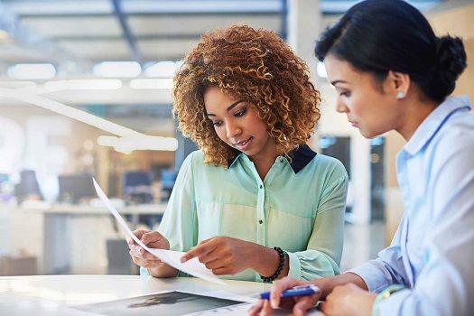 Two female office workers reviewing a document for errors