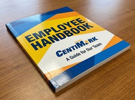An employee handbook for the Centimark company lies on a walnut table