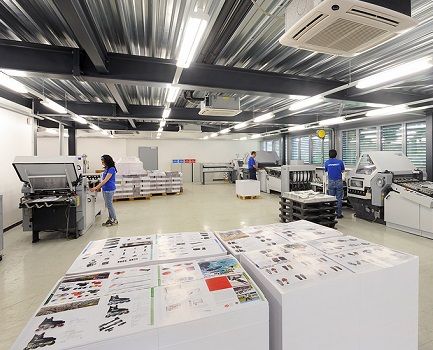 A commercial print facility with two workers and stacks of printing