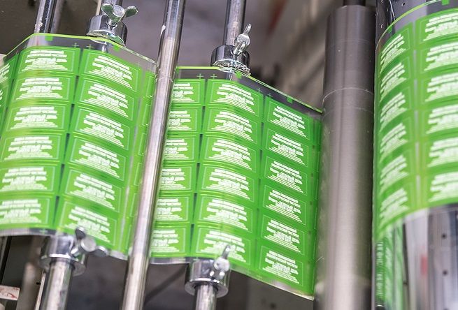 Green and white labels moving through the rollers of a printing press