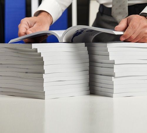 A man opening a perfect bound book near two stacks of perfect bound books