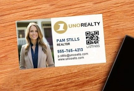 A business card for a female realtor lying on a desk next to a cell phone